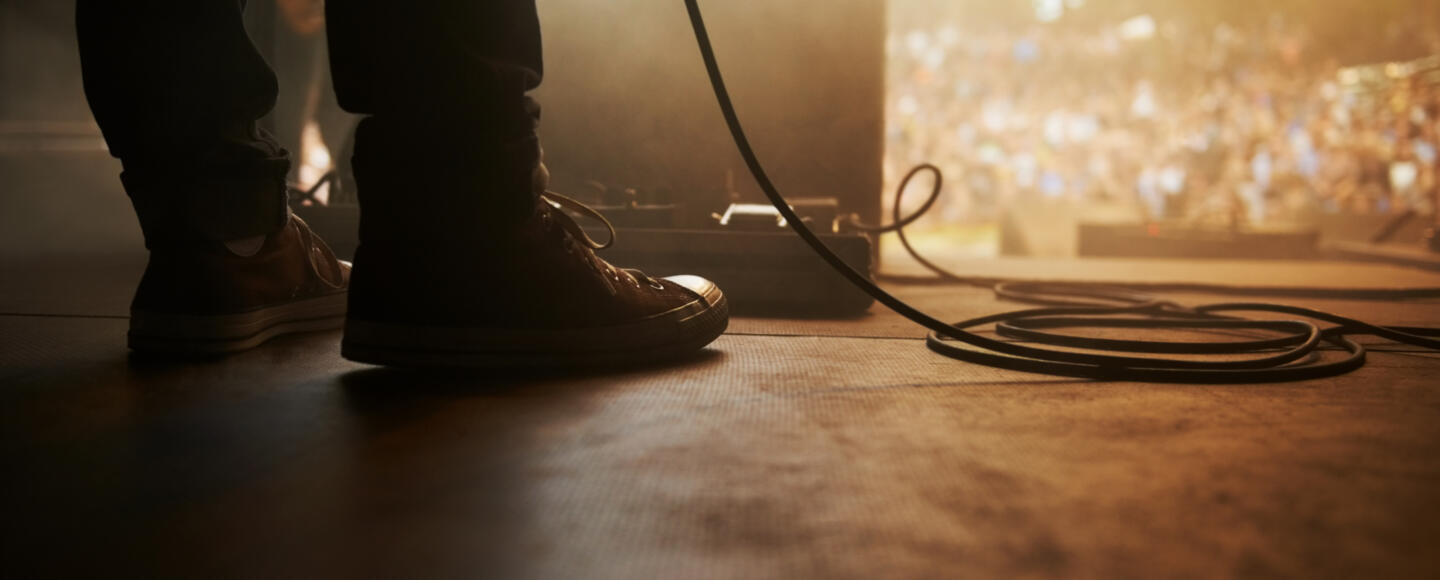 A musician's boots next to a microphone cable standing in front of an outdoor festival audience