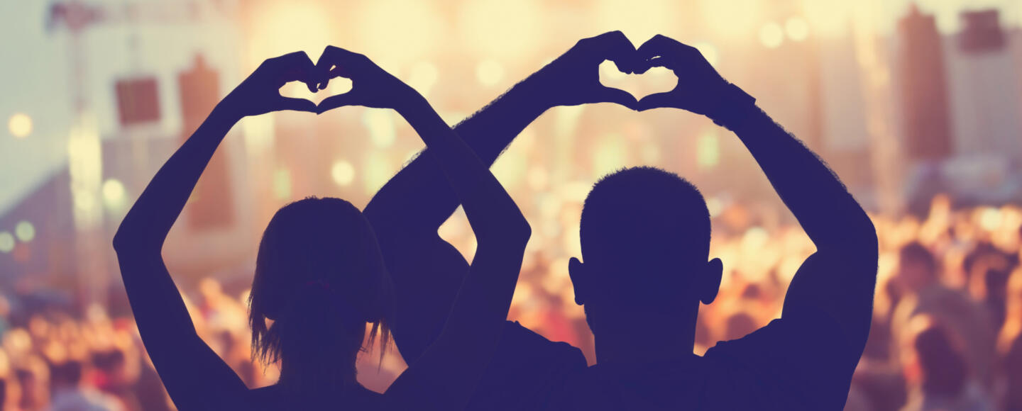 Two people making heart shapes with their hands at an outdoor gig